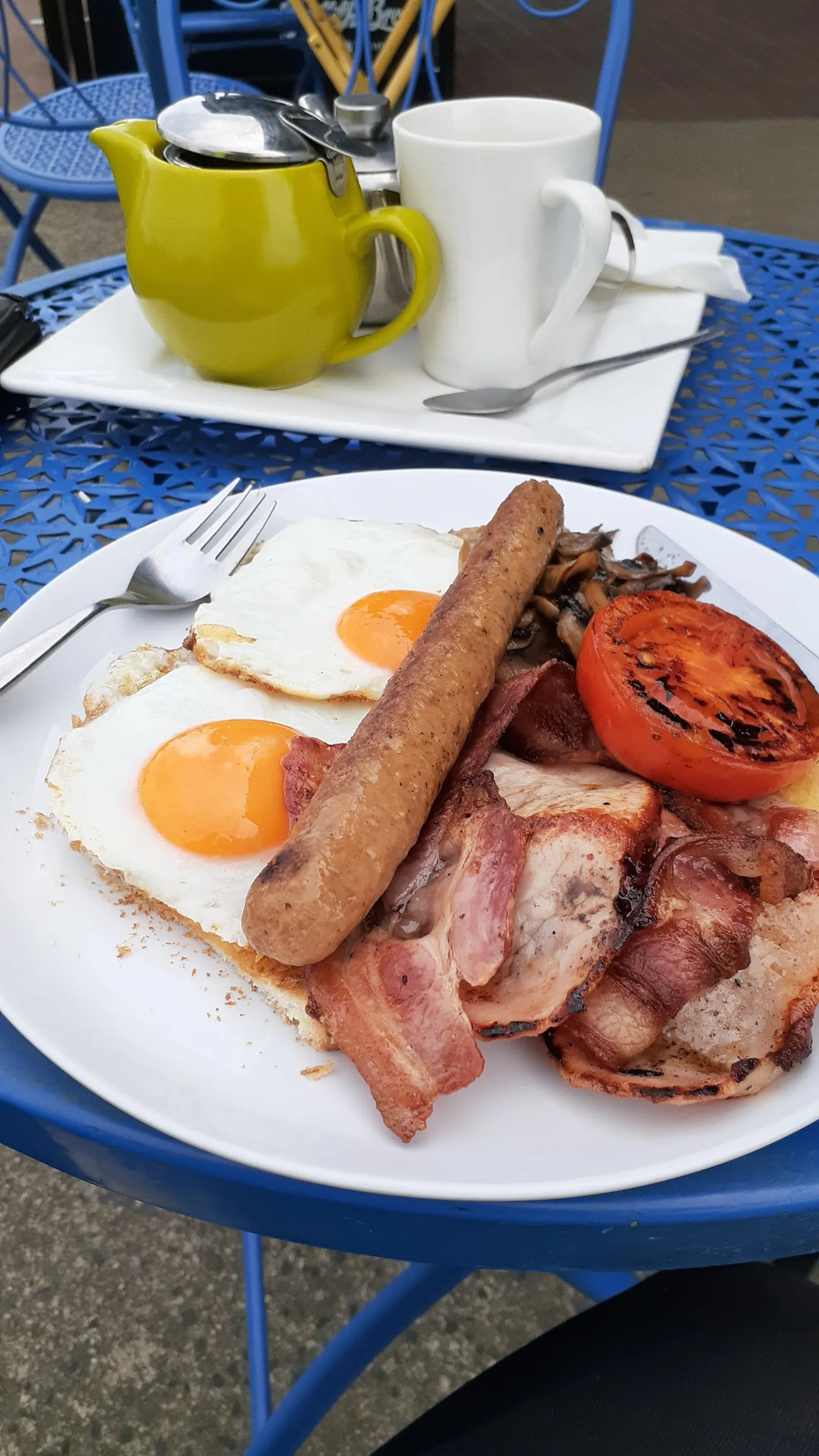 Full cooked breakfast with fried eggs and bacon on blue outdoor table at Grantville Bakehouse