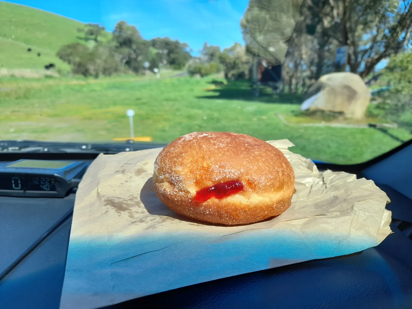 Jam donut on car dashboard with green paddock and blue sky backdrop on a country drive