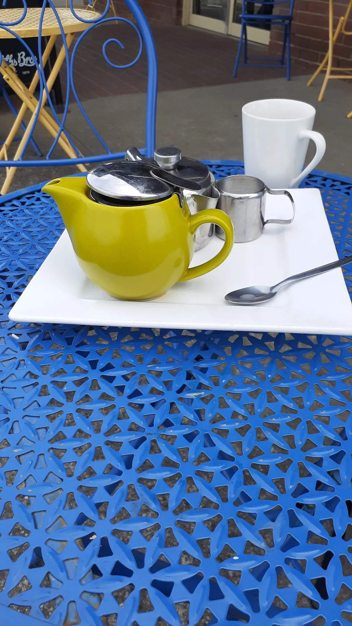Yellow teapot and white mug on white tray at blue outdoor table