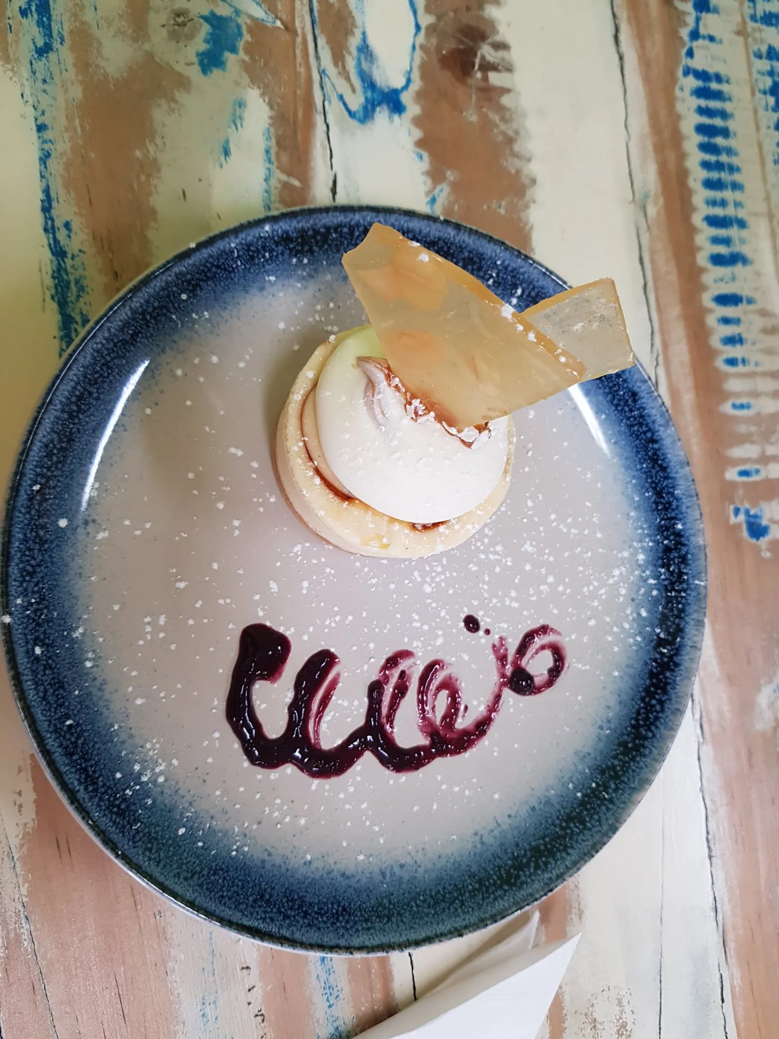 Dessert tart with cream filling and berry sauce on decorative blue ceramic plate