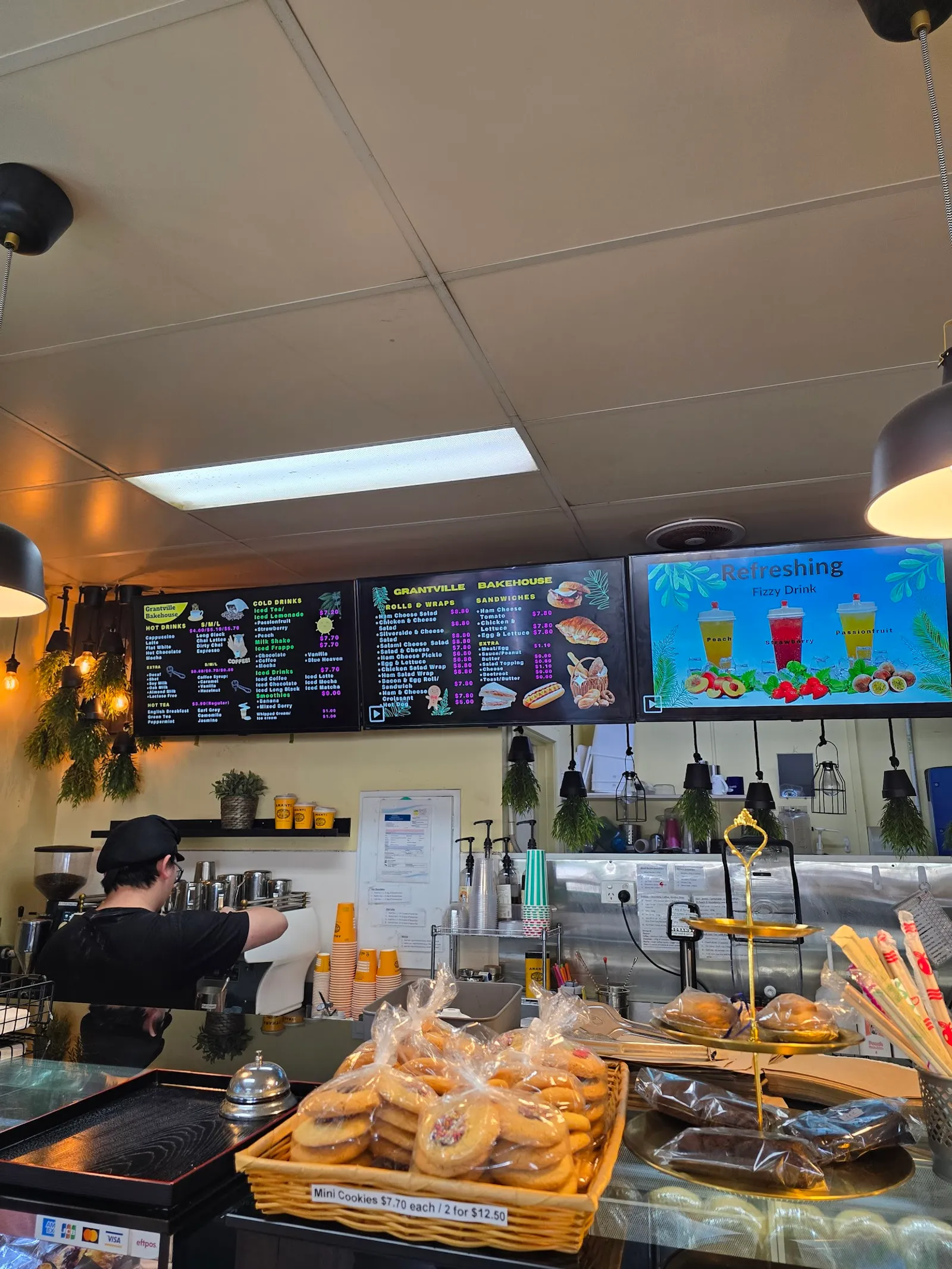 Staff member at coffee machine with digital menu board and pastries at Grantville Bakehouse counter